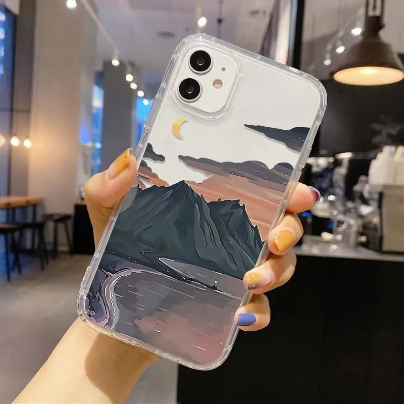a woman holding up a phone case with a mountain scene on it