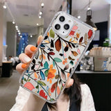 a woman holding up a phone case with colorful leaves on it