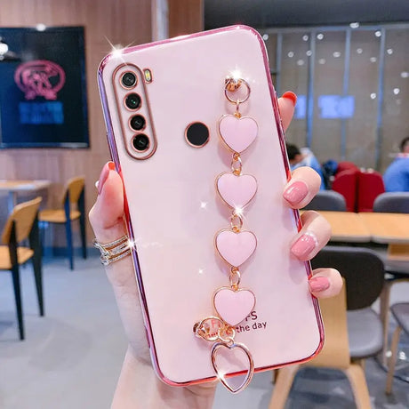 a woman holding a pink phone case with heart charms