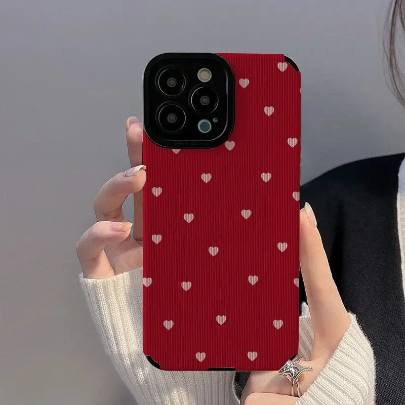 a woman holding up a red phone case with hearts on it