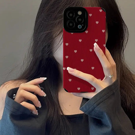 a woman holding up a red phone case with hearts on it