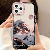 a woman holding a phone case with mountains in the background