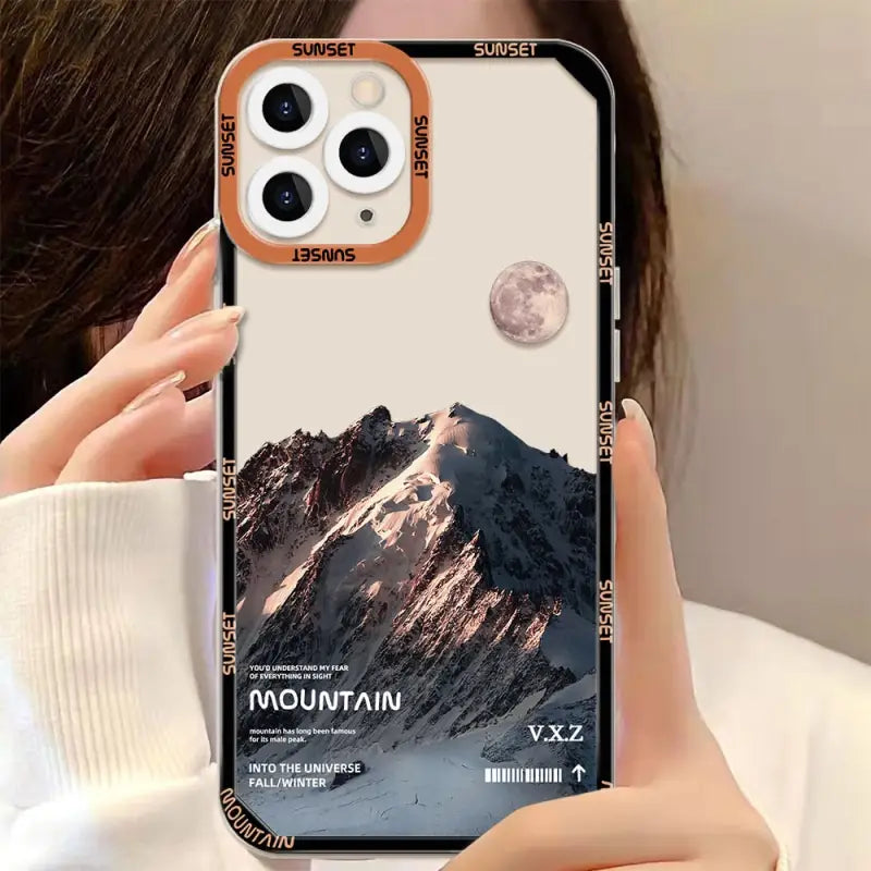 a woman holding up a phone case with a mountain scene