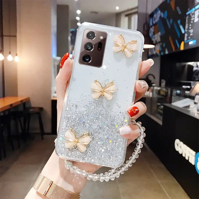a woman holding up a phone case with glitter butterflies