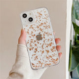 a woman holding a phone case with a white and gold glitter design