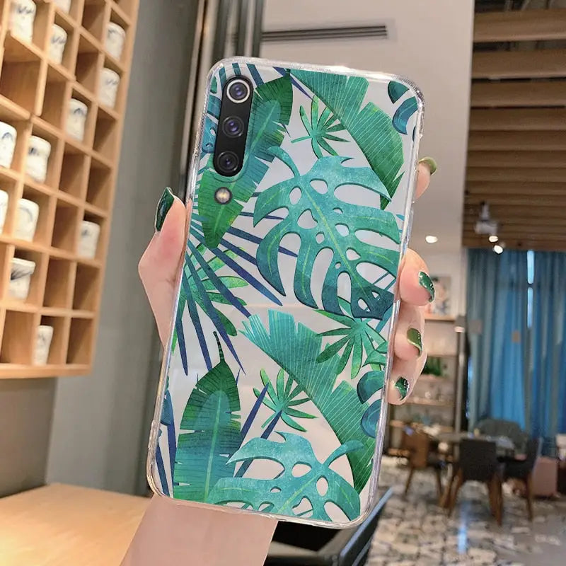 a woman holding up a phone case with a green leaf print