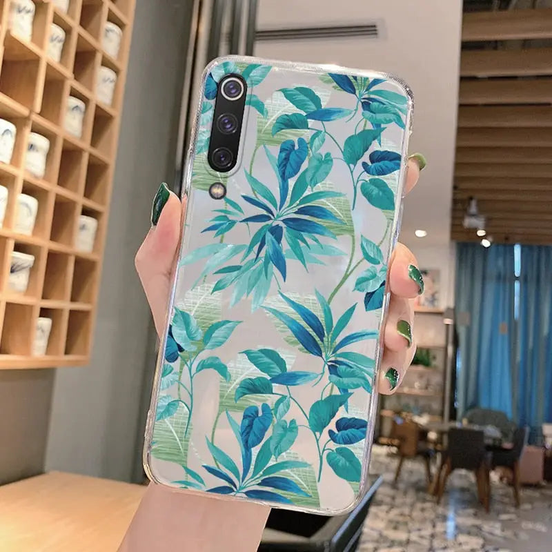 a woman holding up a phone case with a blue and green leaf print