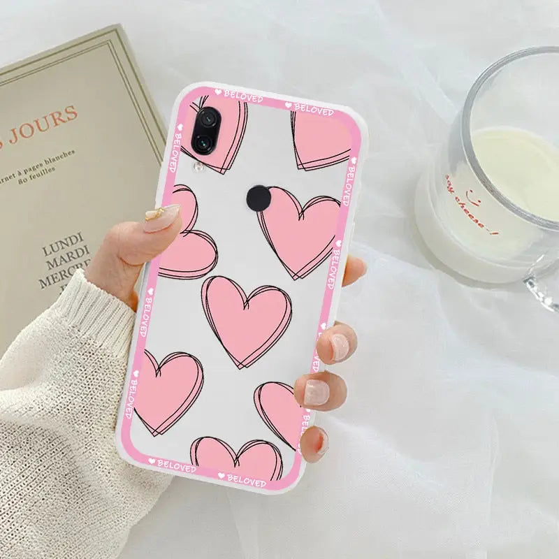 a woman holding a pink phone case with hearts on it