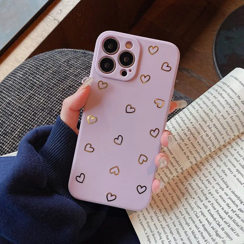 a woman holding a pink phone case with gold hearts