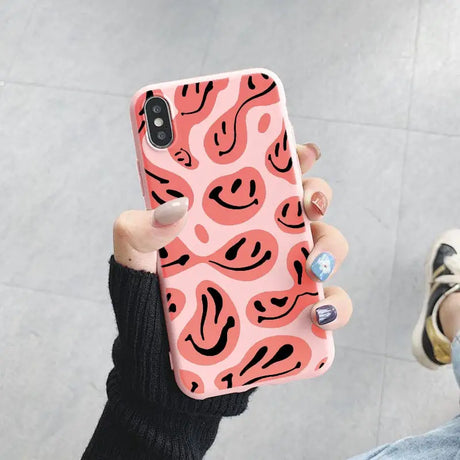 a woman holding up a pink phone case with black and white shapes