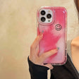 a woman holding a pink phone case with a smiley face on it