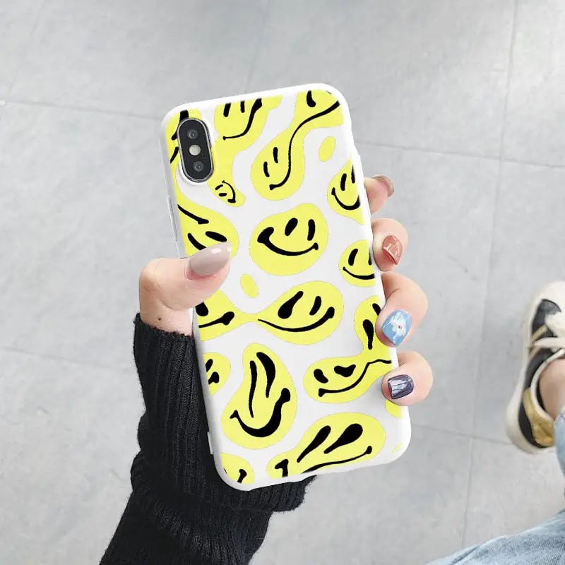 a woman holding up a yellow and black smiley face phone case