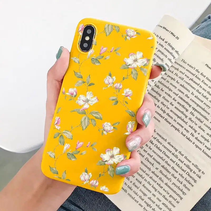 a woman holding a yellow phone case with flowers on it