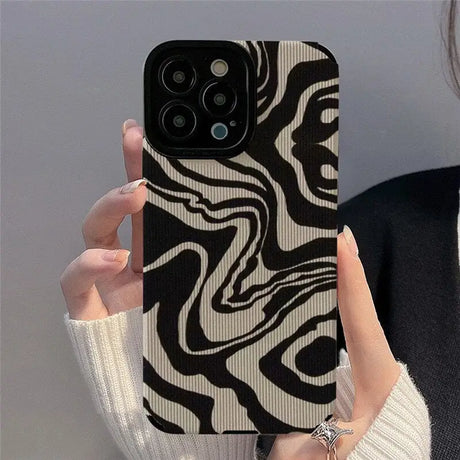 A woman holding up a phone case with a black and white pattern