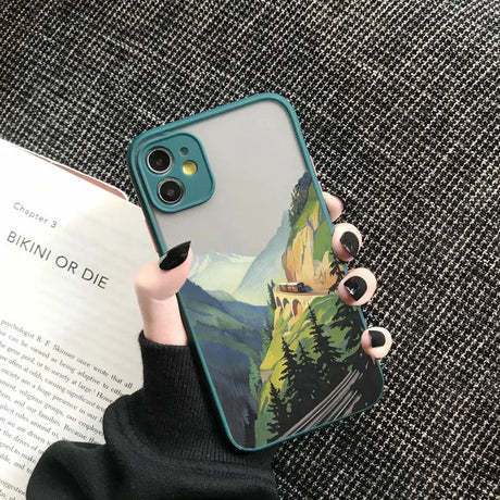 A woman holding a phone case with a painting of a mountain scene