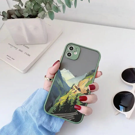 A woman holding a phone case with a painting of a mountain scene