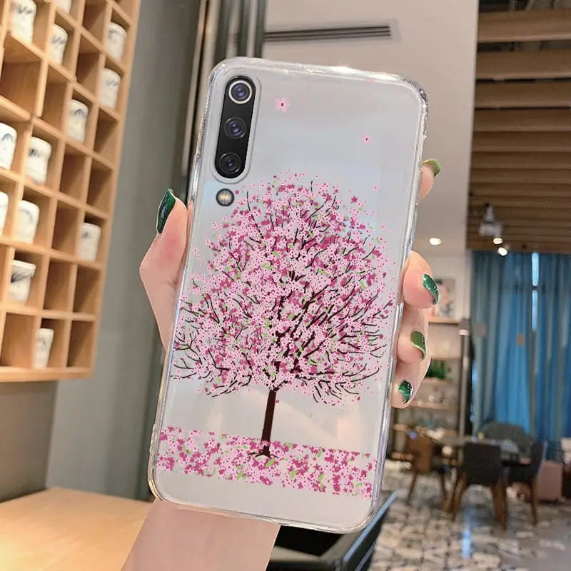 a woman holding a phone case with a pink cherry tree on it