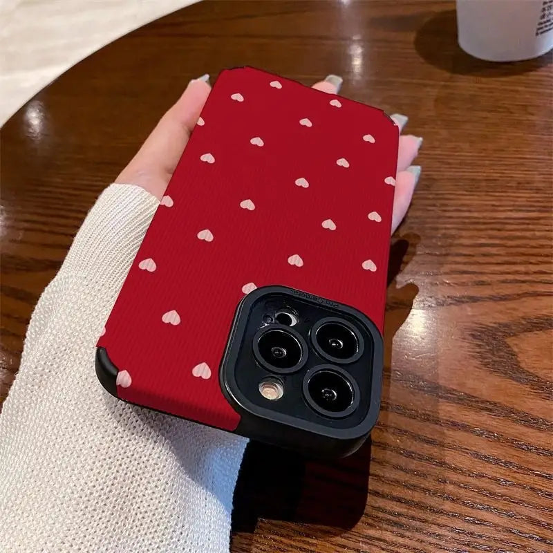 a woman holding a red phone case with white hearts on it