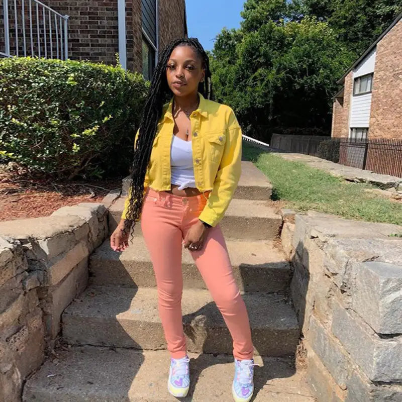 a woman standing on a sidewalk wearing a yellow jacket and pink pants