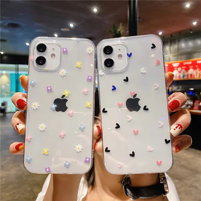 a woman holding up two iphone cases with flowers and hearts