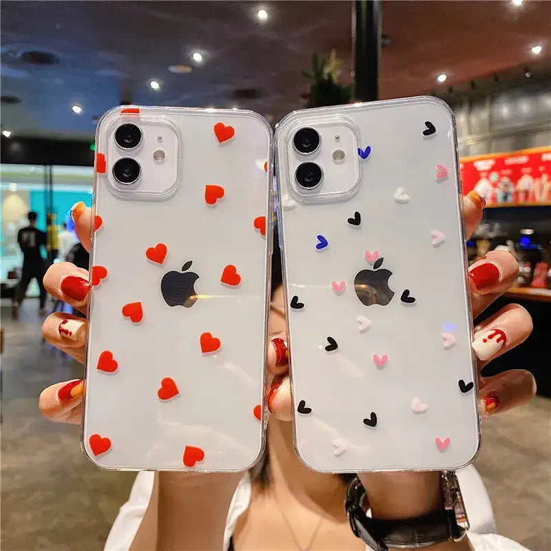 a woman holding up two iphone cases with hearts on them