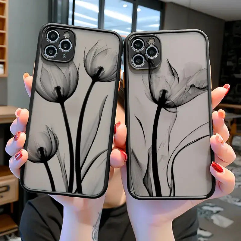 a woman holding up two iphone cases with black and white flowers