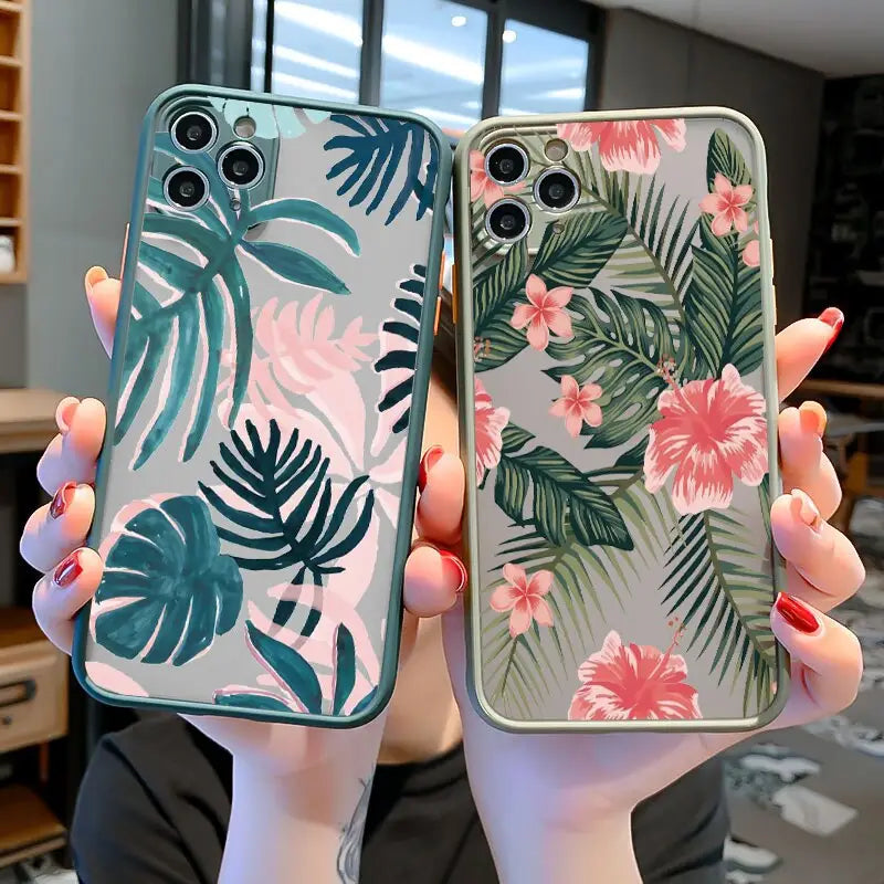 a woman holding up two iphone cases with tropical leaves and flowers
