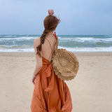 a woman in an orange dress and straw hat walking on the beach