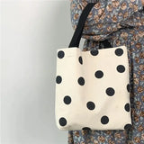 a woman holding a white and black polka dot tote bag