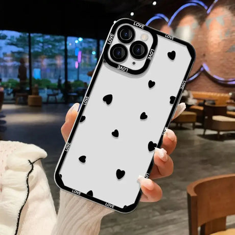 A woman holding up a white iphone case with black hearts