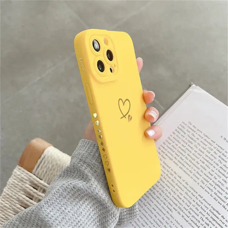 a woman holding a yellow phone case with a heart drawn on it