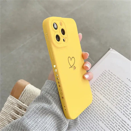 A woman holding a yellow phone case with a heart drawn on it