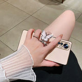 a woman’s hand holding a phone with a butterfly ring