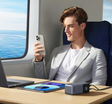 Young man in a white suit jacket using a smartphone while seated at a table with electronic devices.